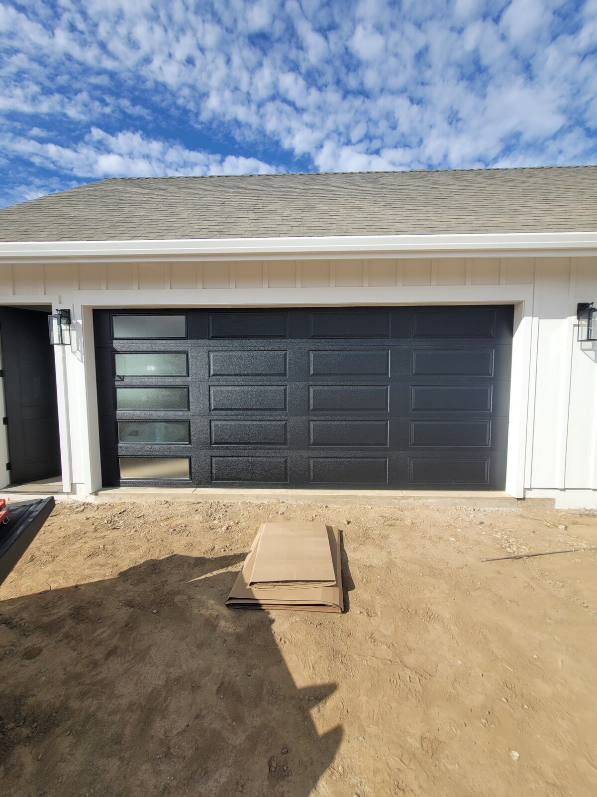 Two modern charcoal garage doors on a white board-and-batten home