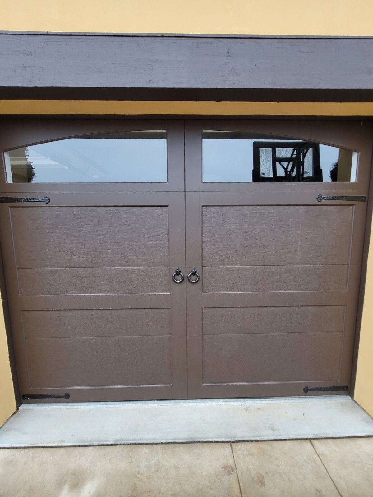 Brown carriage-style garage door with arched window inserts